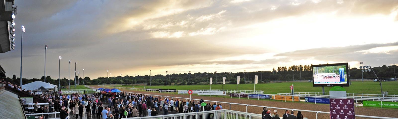 Floodlights come on as dusk begins to settle over the crowd at Wolverhampton Racecourse.