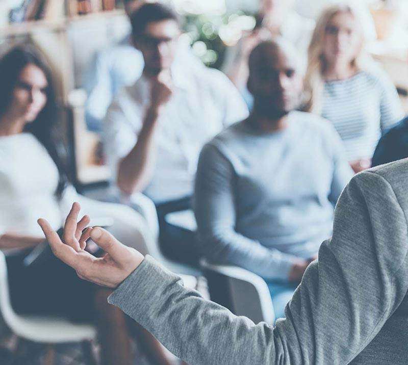 Group of people sitting at a conference, listening to a presenter.
