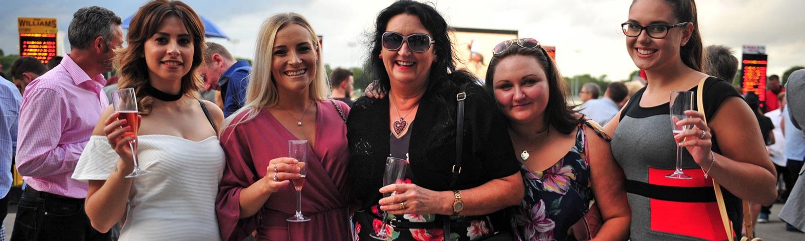 Group of ladies holding champagne glasses, attending races.